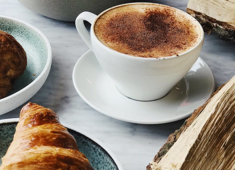 Petit-déjeuner, café dans une tasse blanche avec un croissant. Décoration avec une buche de bois près de la tasse à café