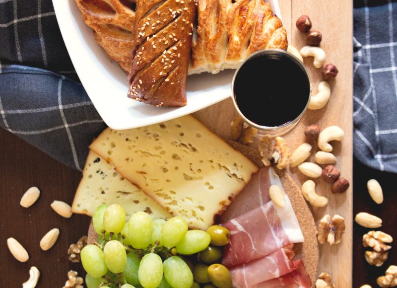 planche ne bois avec du raisin vert, des viennoiseries, du jambon cru et des tranches de fromage